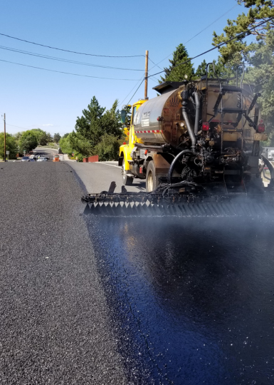 A bitumen spray truck applying a tack coat before laying fresh asphalt on a road under construction.